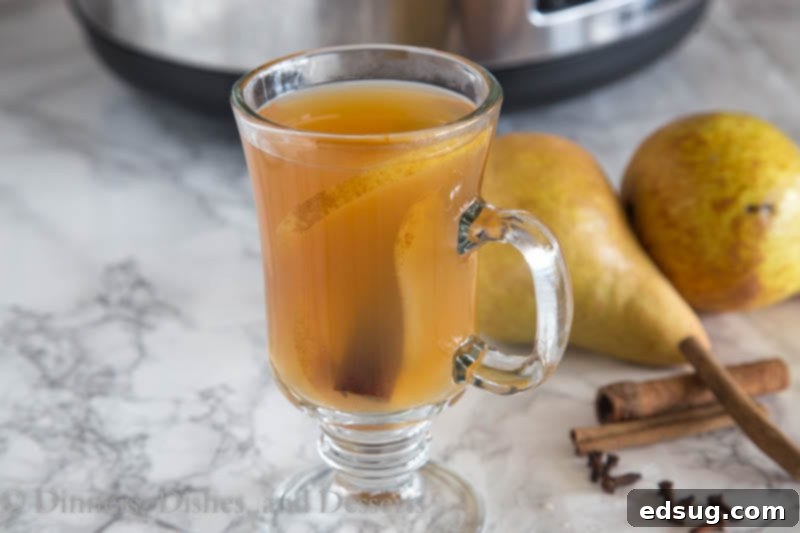 Spiced Pear Nectar 3 Two mugs of spiced pear cider on a wooden table, with fresh pear slices, cinnamon sticks, and star anise scattered around for garnish.