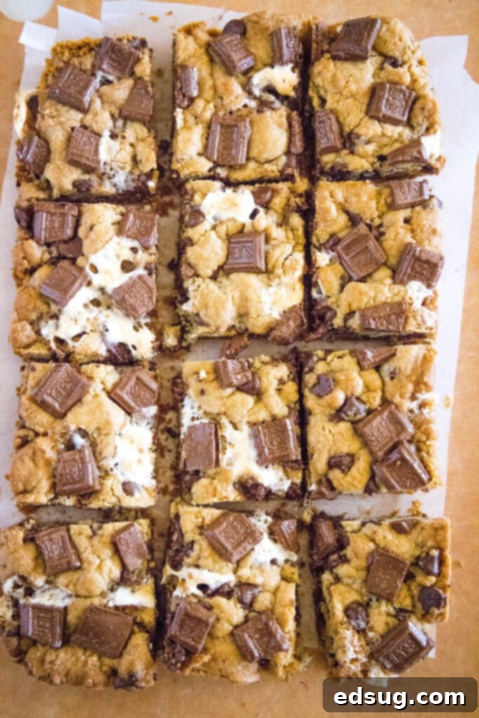 Looking down on perfectly sliced S'mores Cookie Bars on a cutting board, showcasing layers of graham cracker crust, chocolate chip cookie, and melted marshmallows.