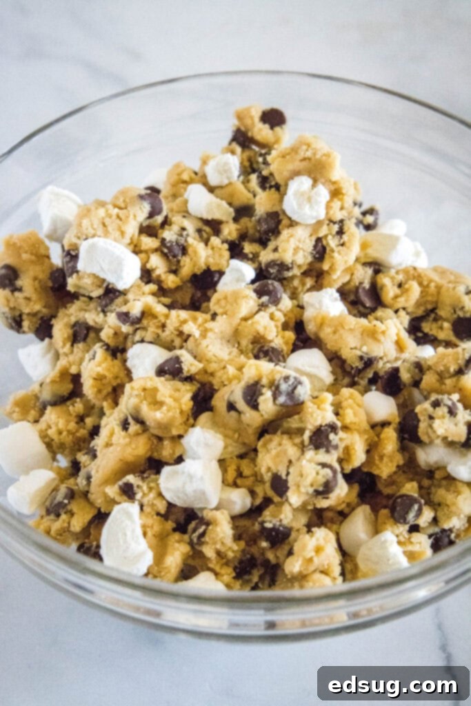 Cookie dough with mini marshmallows and chocolate chips in a mixing bowl, ready to be spread into the pan.