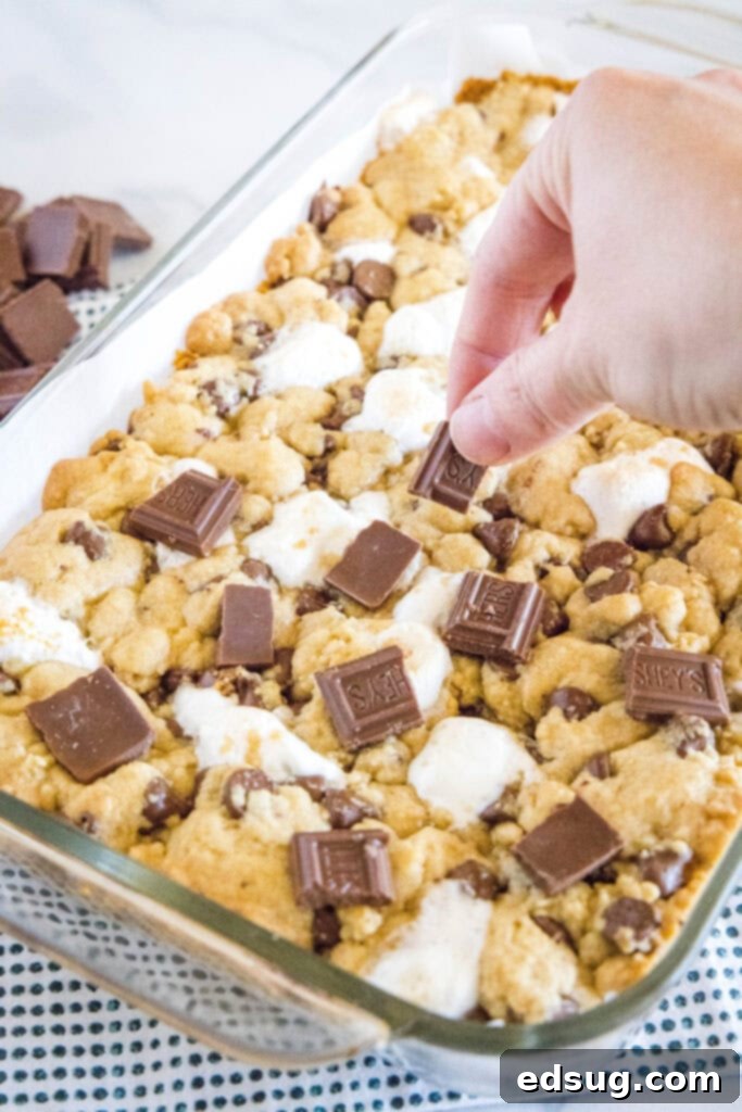 Arranging broken Hershey's chocolate bar pieces on top of partially baked cookie dough in a baking pan.