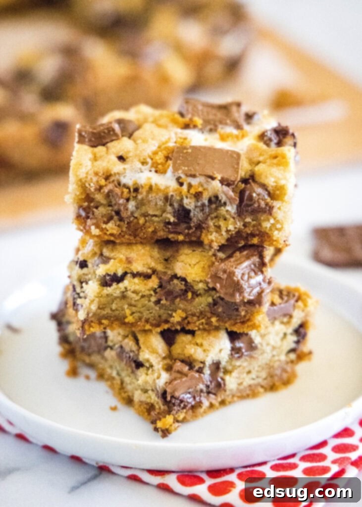 Stacked S'mores Cookie Bars on a white plate, showing the thick layers of cookie, marshmallow, and chocolate.