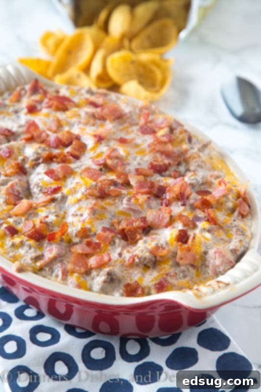 Ultimate Bacon Cheeseburger Dip 4 A person scooping a generous portion of Bacon Cheeseburger Dip with a Fritos scoop chip, showcasing the gooey, melted cheese and hearty ingredients.