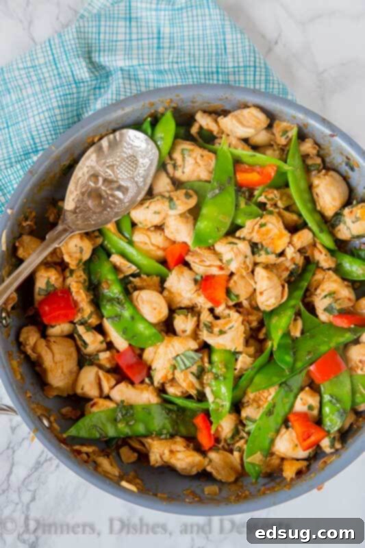 Fiery Basil Chicken 5 Spicy basil chicken stir-frying in a large wok, with sauce thickening around the chicken and vegetables.