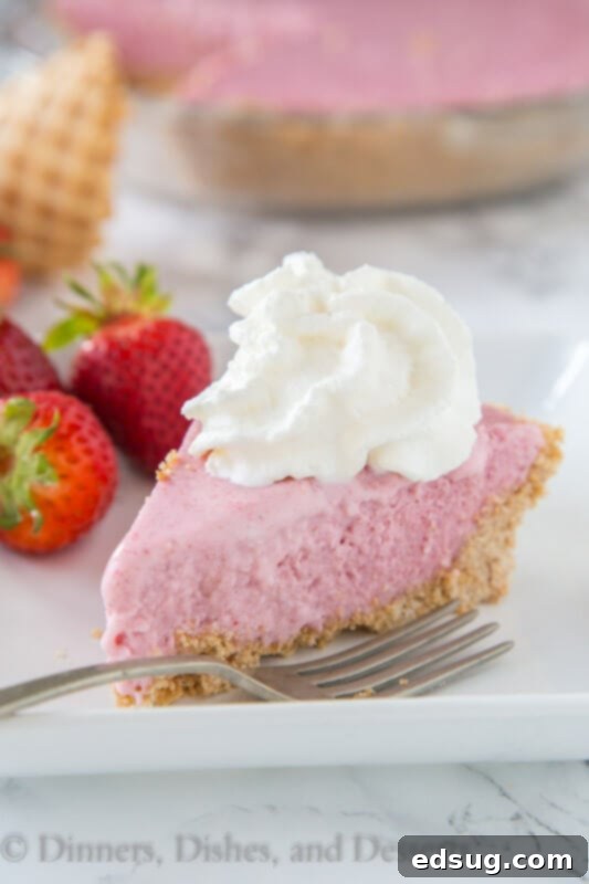 Dreamy Strawberry Milkshake Pie 2 A slice of creamy strawberry milkshake pie on a white plate, garnished with fresh strawberries and whipped cream