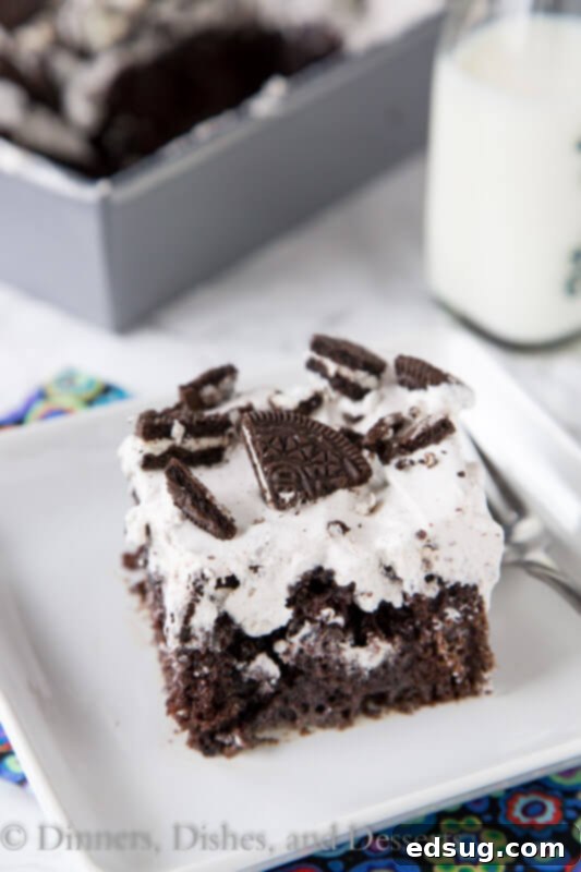 Close-up of a large piece of Oreo Poke Cake with a fork, ready to eat.