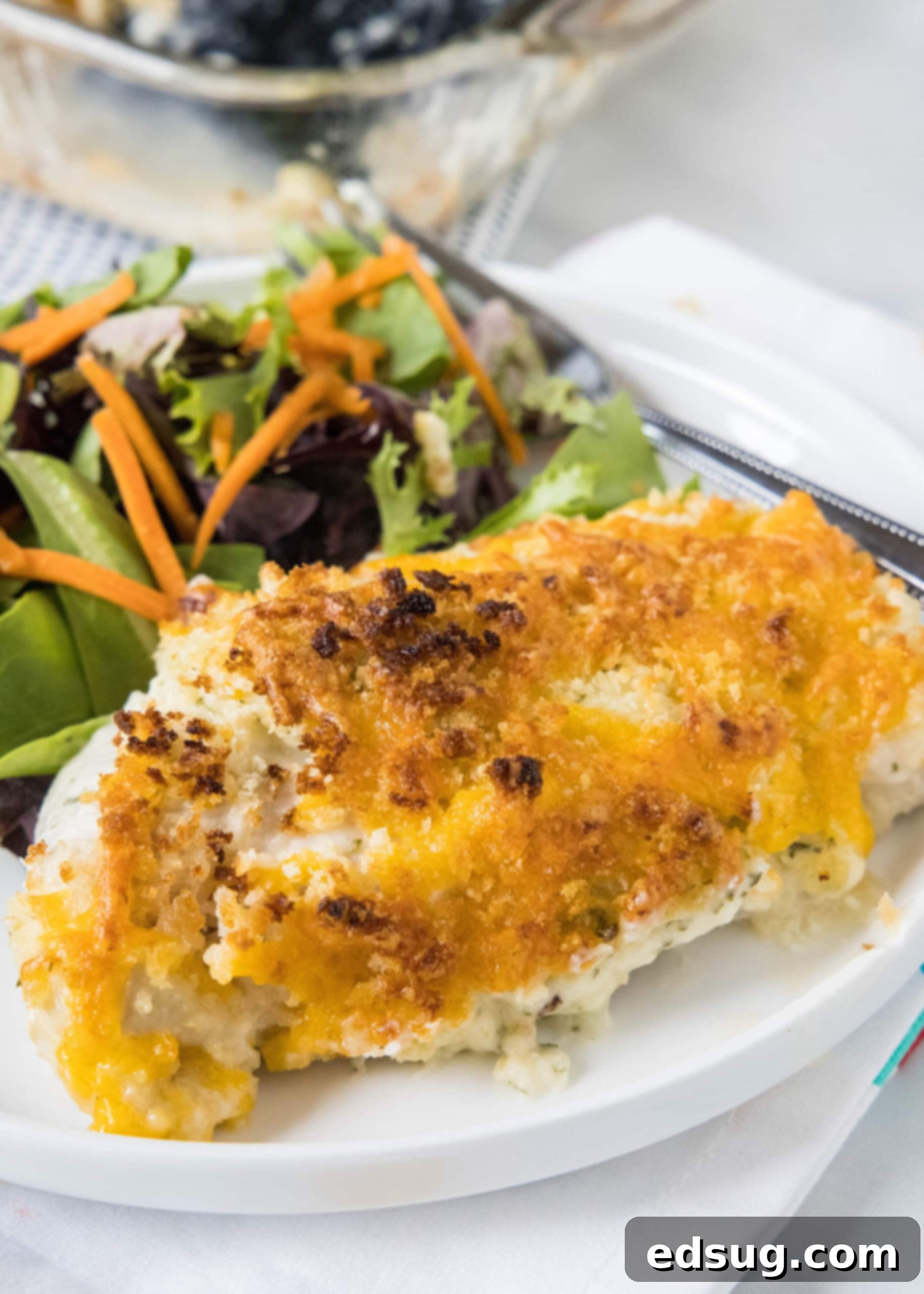 Baked ranch chicken served with a side of salad on a white plate.
