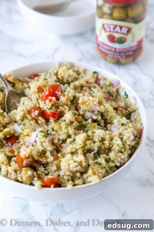 Zesty Mediterranean Quinoa Bowl 5 Mediterranean quinoa salad in a wooden bowl with a serving spoon, garnished with fresh herbs.