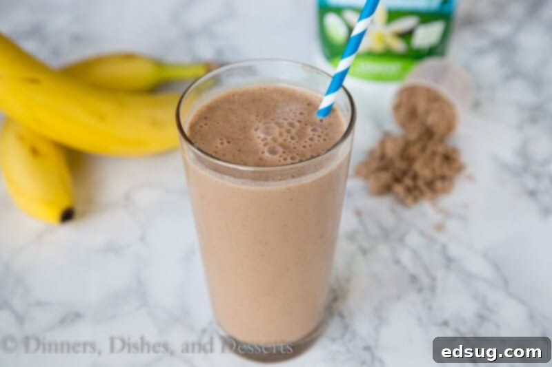 Ultimate Chocolate Peanut Butter Smoothie 3 Close-up of a chocolate peanut butter smoothie in a clear glass with a spoon, showing its creamy texture.