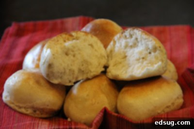 Basket of freshly baked homemade herb dinner rolls, one broken in half to show its soft interior.