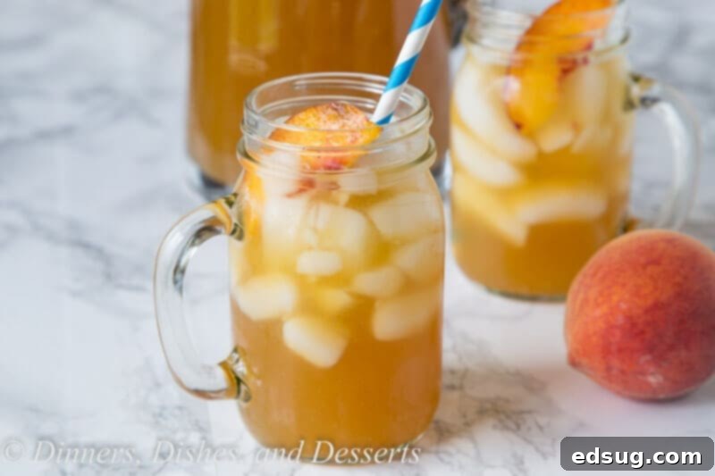 Refreshing Peach Tea Punch 3 A refreshing glass of peach tea punch, garnished with fresh peach slices and mint, against a sunny outdoor backdrop.