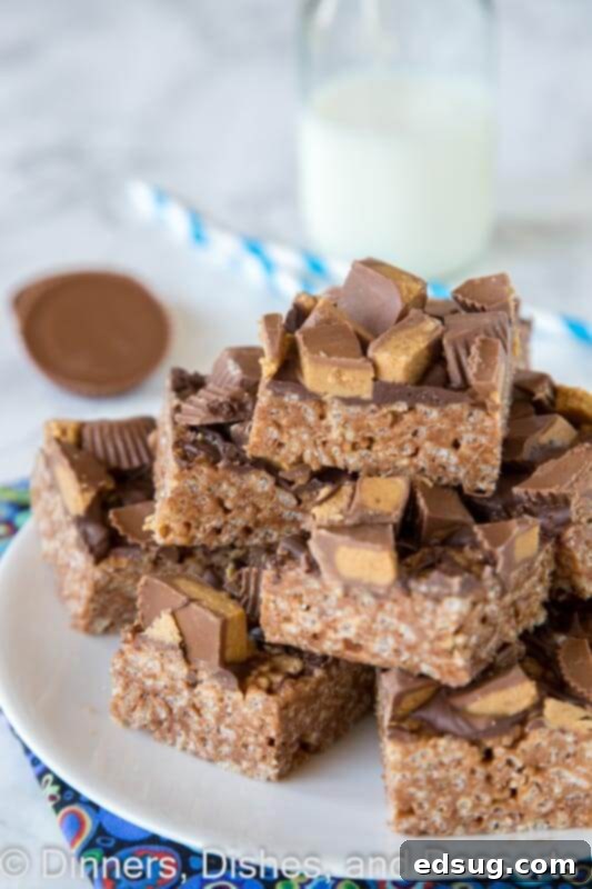 Irresistible Reese's Peanut Butter Krispie Treats 2 A stack of Reese's Peanut Butter Rice Krispie Treats with chocolate drizzle and peanut butter cup pieces on a white plate