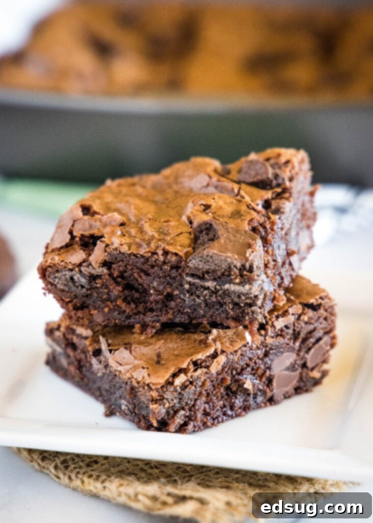Decadent Thin Mint Brownies 2 Thin Mint Brownies stacked on a white plate, showcasing their fudgy texture and mint cookie pieces