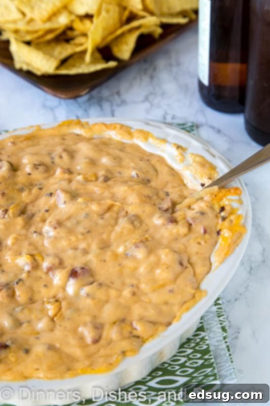 Loaded Cheddar Brat Dip 2 A serving bowl filled with warm, gooey Cheddar Brat Cheese Dip on a plate, ready for game day snacking