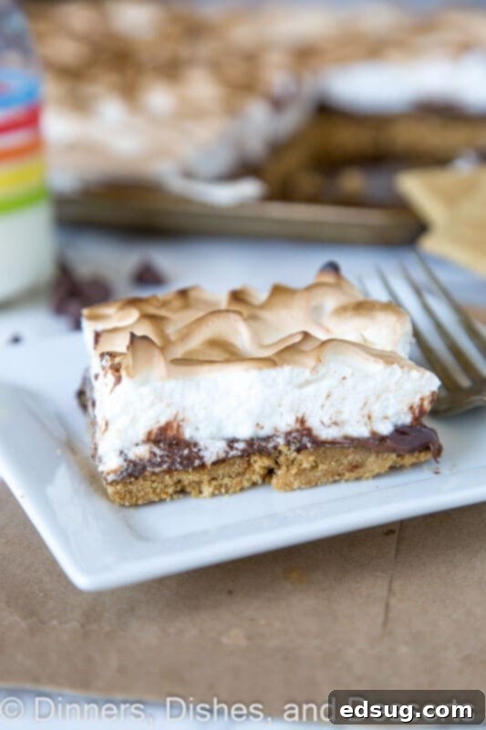 Sheet Pan S'mores Tart 2 A slice of sheet pan s'mores tart on a white plate, showing the layers of crust, chocolate, and toasted meringue.
