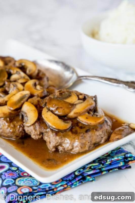 A serving of hamburger steaks with mushroom gravy, garnished with fresh herbs, ready for a comforting meal.