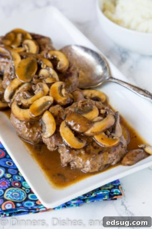 A beautifully plated serving of hamburger steaks and mushroom gravy, alongside green beans and mashed potatoes, highlighting a complete meal.