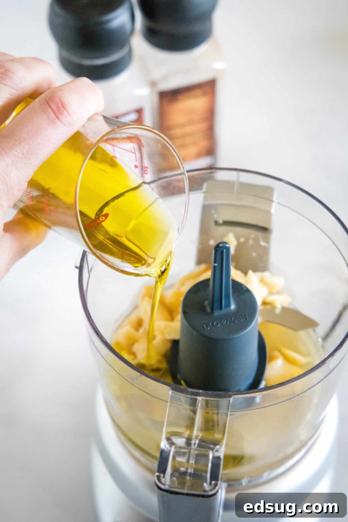 Pouring golden extra virgin olive oil into a food processor with other vinaigrette ingredients