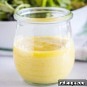 Close-up of a glass jar filled with a creamy, rich roasted garlic vinaigrette, part of the recipe card