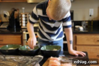 Adult Essentials 5 A young boy, around 5 years old, intently using small tongs to dip a piece of chicken into a bowl of breading, demonstrating a hands-on cooking activity.