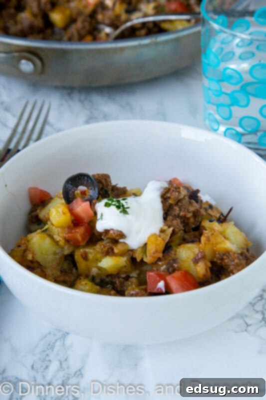 A serving of Mexican skillet potatoes with fresh avocado slices and a dollop of sour cream on a white plate, ready to be eaten.