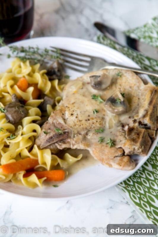Close-up of a plate with slow cooker pork chops, tender vegetables, and a creamy sauce, garnished with fresh herbs.