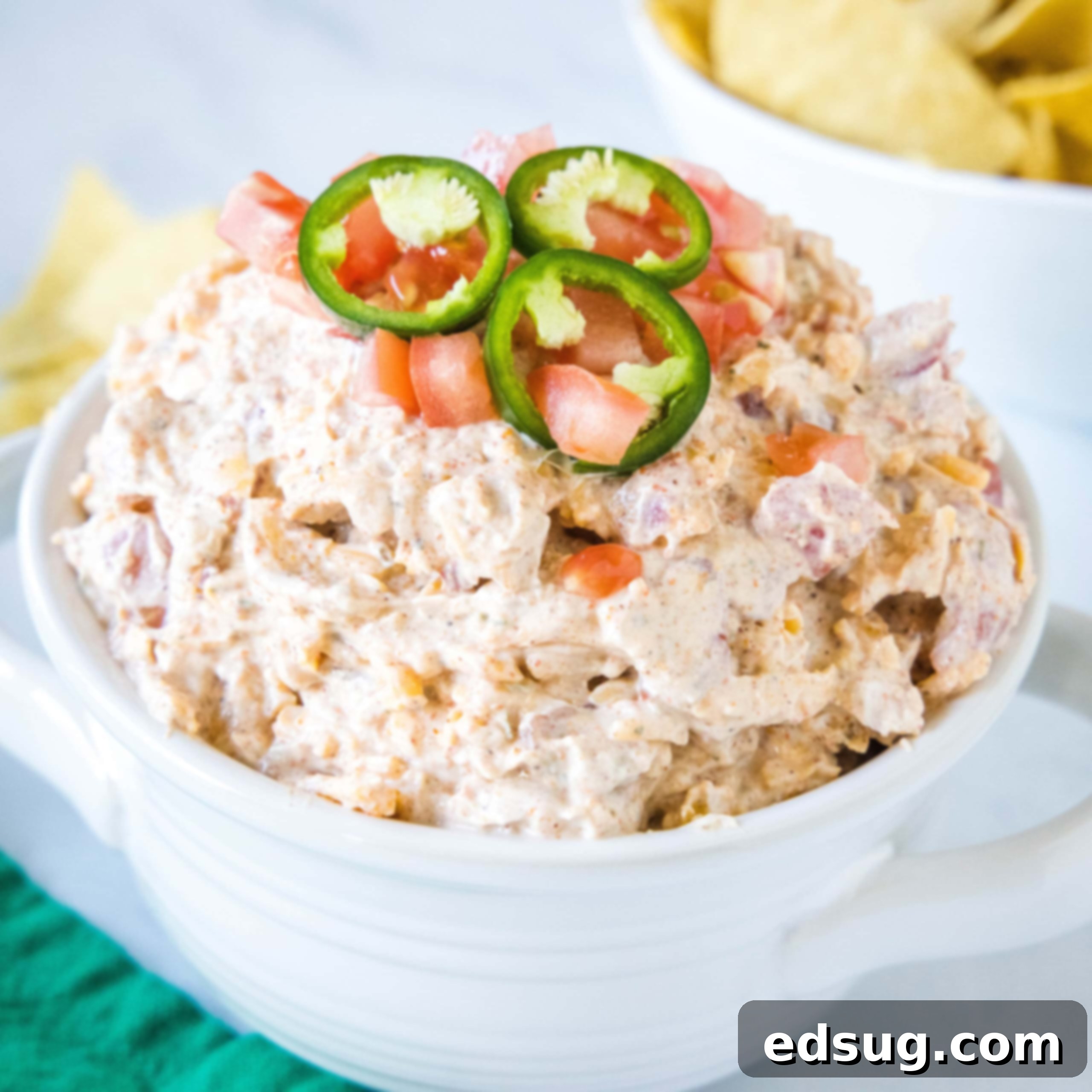 Kickoff Comfort Food 13 Boat dip topped with sliced jalapeños in a white bowl, with a bowl of chips in the background, ready to be served