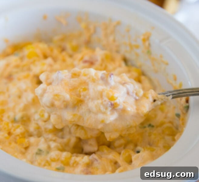 Kickoff Comfort Food 17 Cheesy Corn Dip in a slow cooker with a serving spoon, garnished with fresh herbs