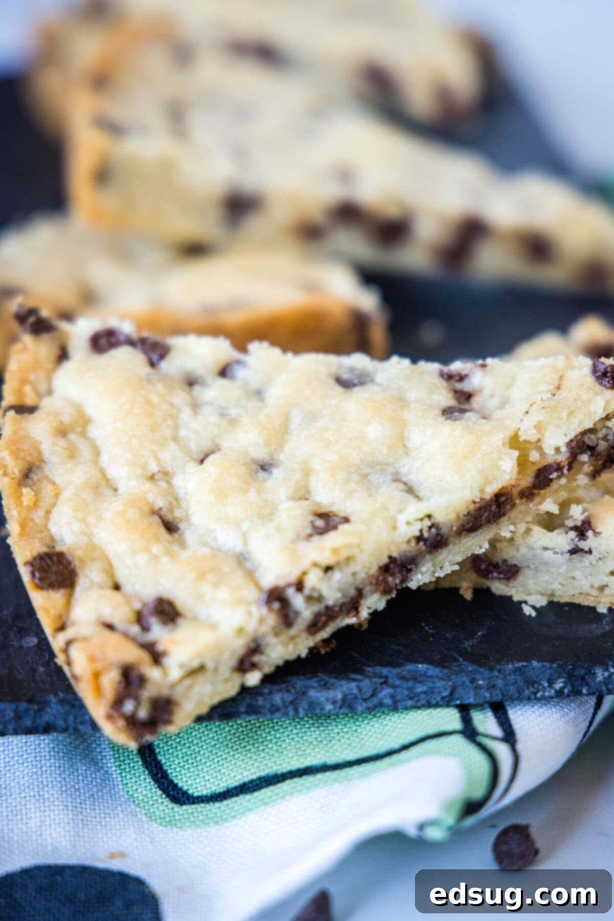 Close up of a stack of two triangular pieces of chocolate chip shortbread, with more pieces in the background.