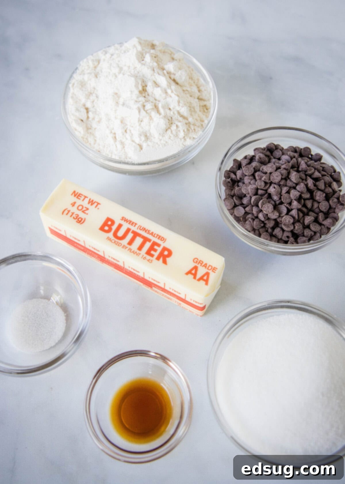 Overhead view of the ingredients needed for chocolate chip shortbread: a bowl of flour, a bowl of sugar, a bowl of chocolate chips, a bowl of salt, a bowl of vanilla, and a stick of butter.