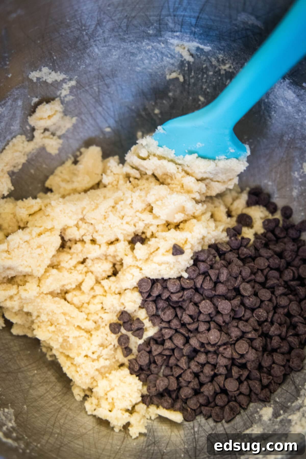 A mixing bowl with shortbread dough, chocolate chips, and a spatula.