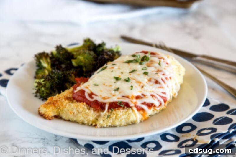 Parmesan-Crusted Baked Chicken 3 A perfectly cooked slice of baked chicken parmesan on a plate, highlighting the golden crust and melted cheese, with a sheet pan in the background.