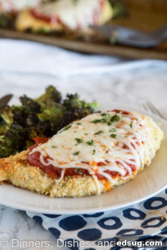 Parmesan-Crusted Baked Chicken 4 A close-up of a plate with baked chicken parmesan, showcasing the crispy crust, melted cheese, and a side of roasted broccoli.