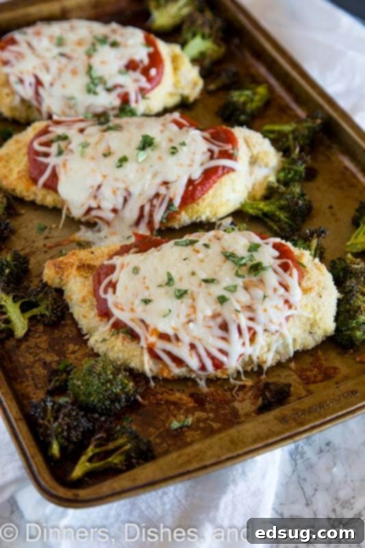Parmesan-Crusted Baked Chicken 5 A baking tray filled with golden-brown baked chicken parmesan pieces topped with melted cheese and rich marinara, alongside perfectly roasted broccoli florets, fresh out of the oven.