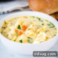 A bowl of creamy chicken tortellini soup with fresh herbs.