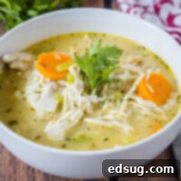 A bowl of chicken rice soup garnished with fresh parsley on a wooden table.