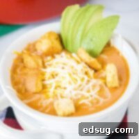 Close up of a creamy cheeseburger soup in a white bowl, topped with cheddar cheese and crispy bacon.