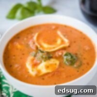 Square image of a rich tortellini soup with vegetables.