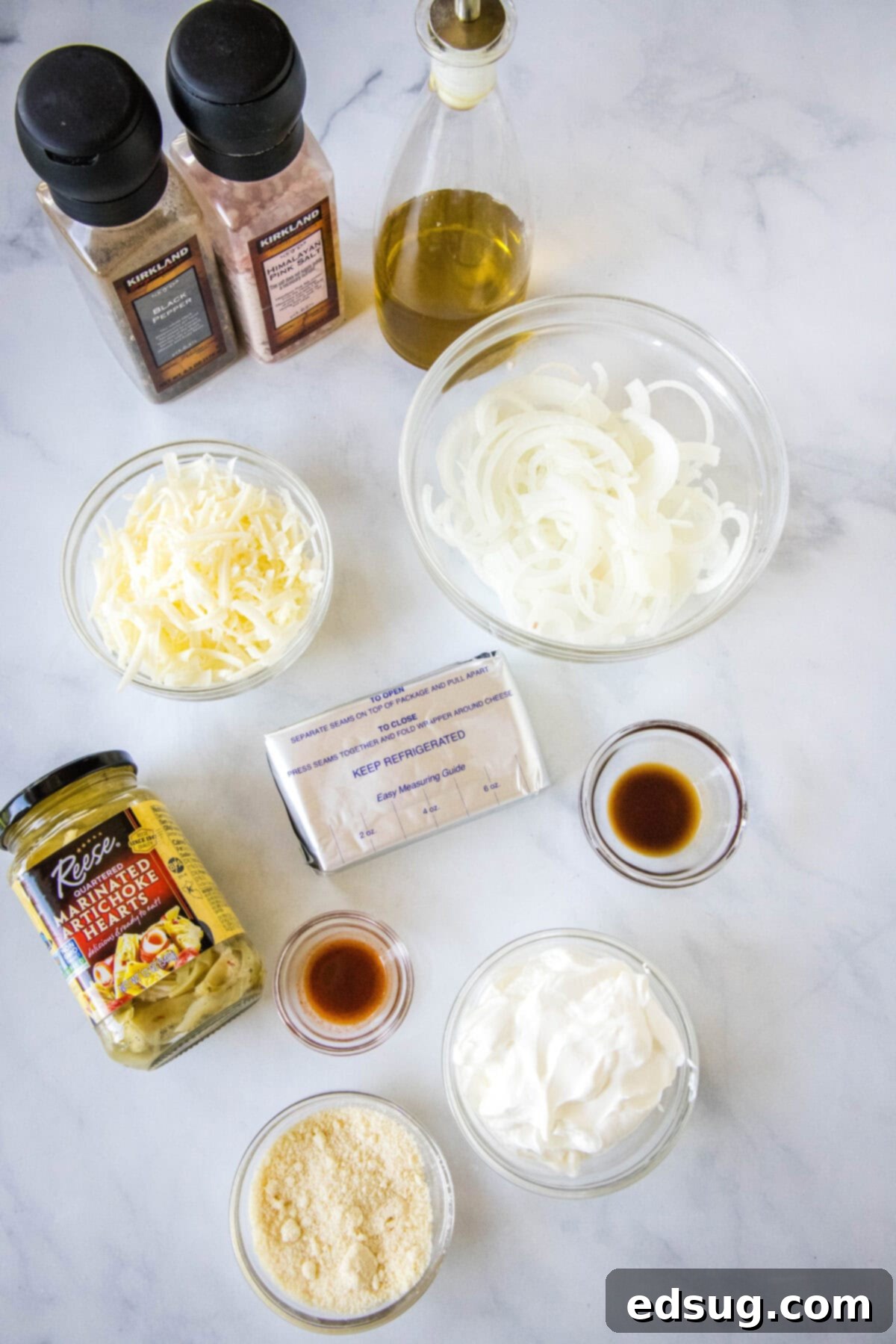 Assortment of fresh ingredients for cheesy artichoke dip including onions, cheeses, and artichoke hearts.