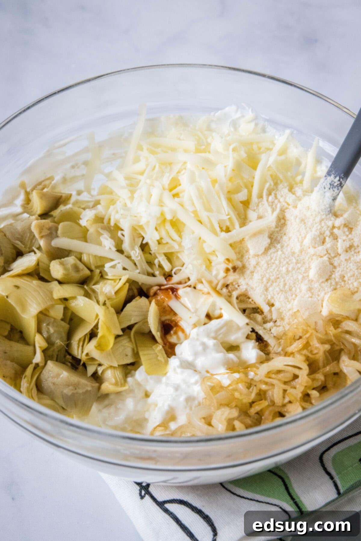 Mixing bowl with cream cheese, sour cream, and other ingredients for cheesy artichoke dip.