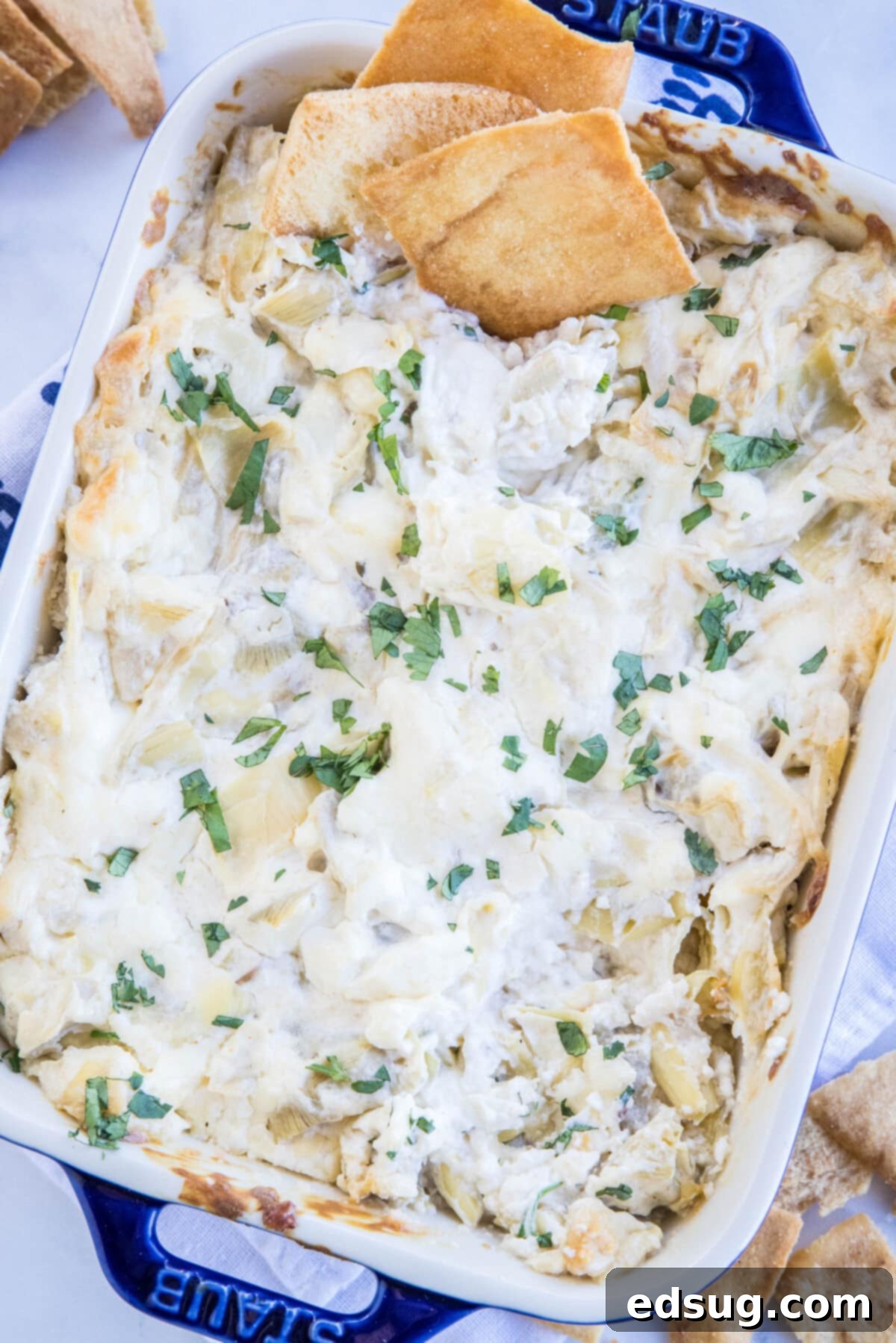 Overhead shot of bubbling cheesy artichoke dip fresh from the oven in a round baking dish.