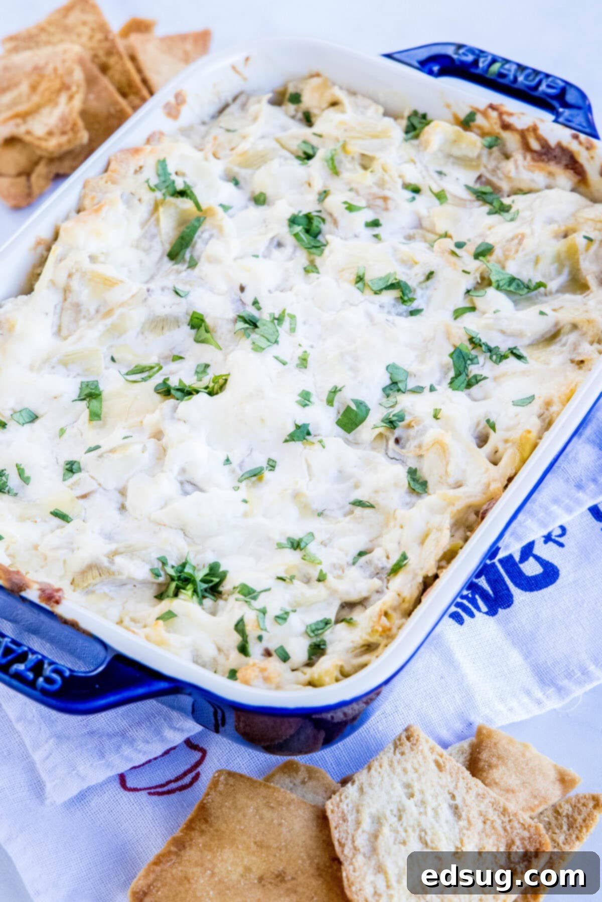 Baking dish with golden-brown cheesy artichoke dip on a rustic wooden table.