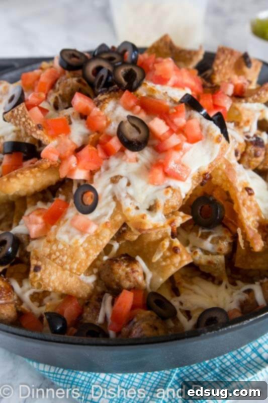 Close-up of a serving of Italian nachos, showcasing the layers of crispy wonton chips, melted mozzarella cheese, and savory Italian chicken sausage, garnished with fresh tomatoes and olives.