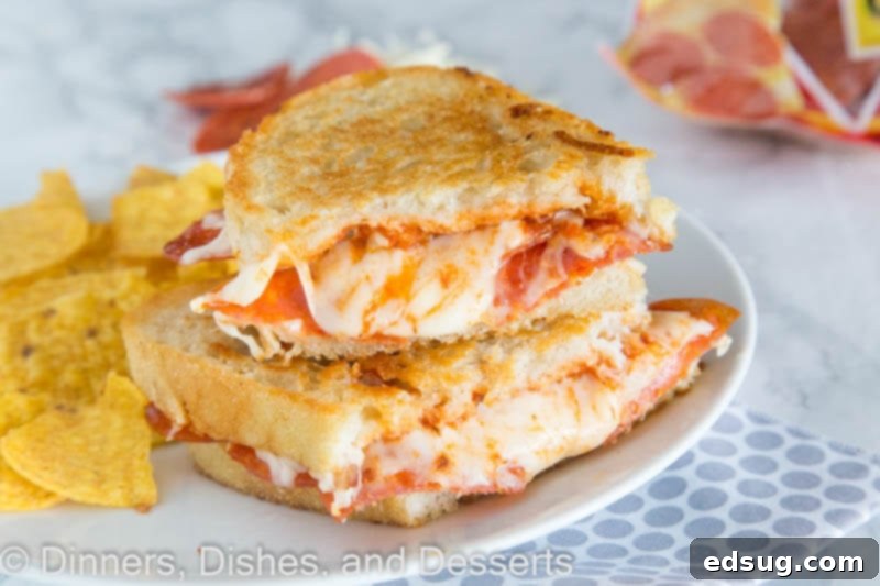 Grilled cheese with pepperoni and melted cheese being cut in half on a wooden board