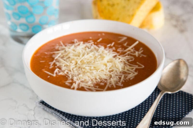 A close-up of creamy tomato soup in a bowl with grated Parmesan cheese melting into it, ready to be served.