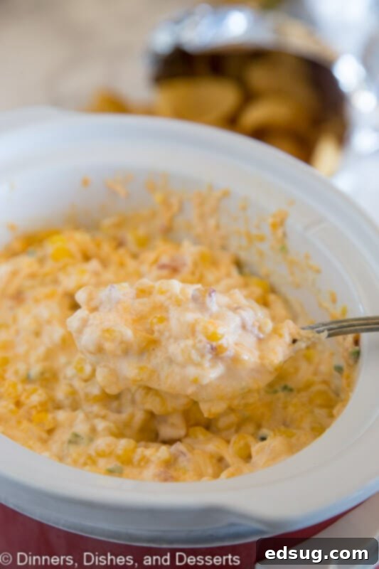 Creamy Cheesy Corn Dip 2 Warm cheesy corn dip served in a slow cooker with a serving spoon, garnished with fresh herbs.