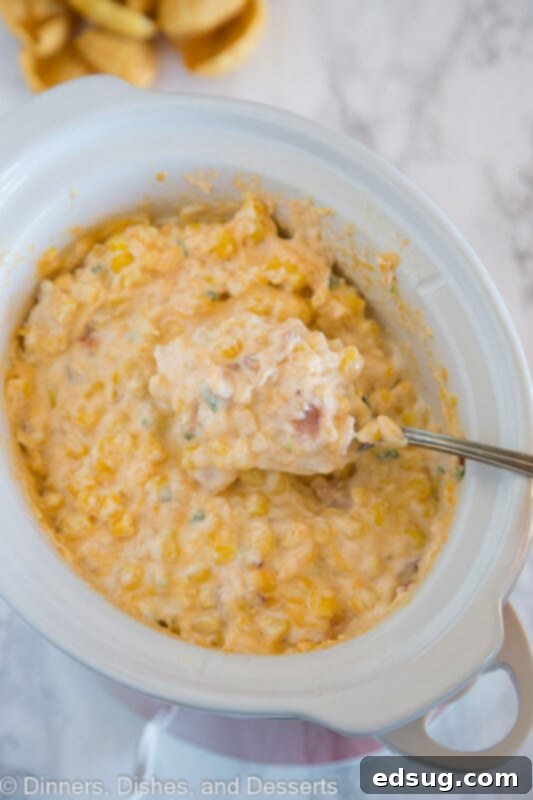 Creamy Cheesy Corn Dip 4 Portion of cheesy corn dip being scooped from a slow cooker onto a plate.