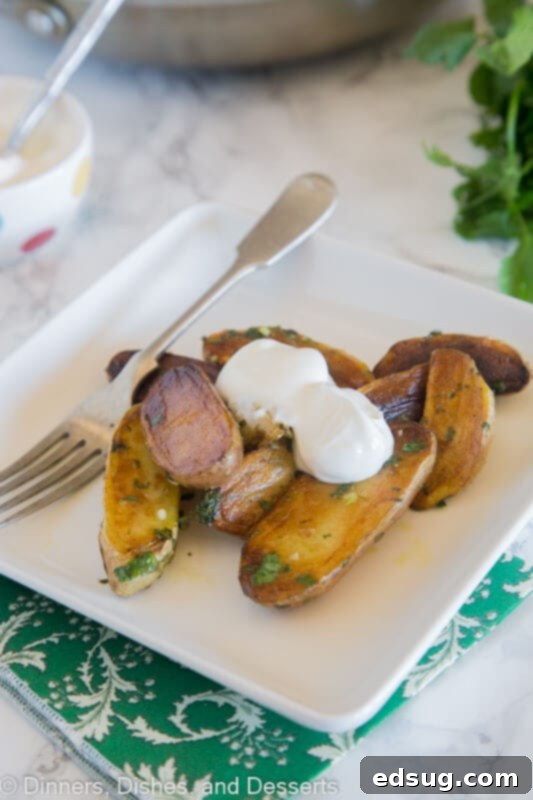 A close-up of Pan-Seared Mojo Potatoes topped with a generous dollop of sour cream and fresh herbs, highlighting their inviting texture and vibrant green sauce.