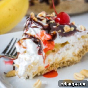 A slice of banana split pie drizzled with chocolate sauce and strawberry sauce, topped with chopped peanuts and cherries on a plate.