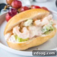 27 Effortless Shrimp Meals 3 A chilled shrimp salad sandwich served on a white plate, accompanied by fresh red grapes.