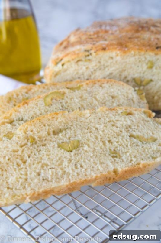 A slice of No-Knead Skillet Olive Bread on a white plate, showcasing the crunchy crust and tender, olive-flecked interior.